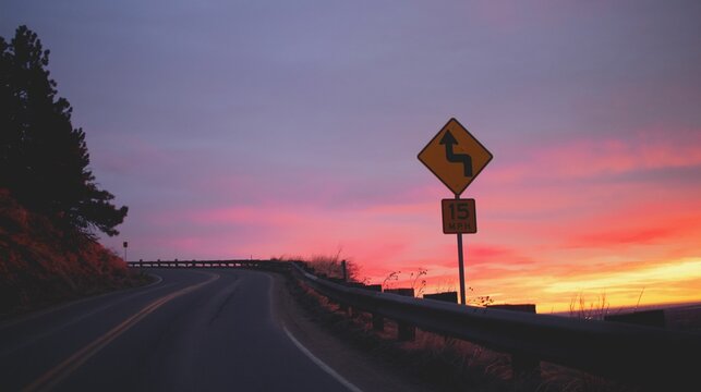 Sunset with a winding road sign.